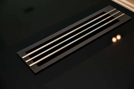 From above of chrome grid covering vent duct in floor reflecting lamp ligh