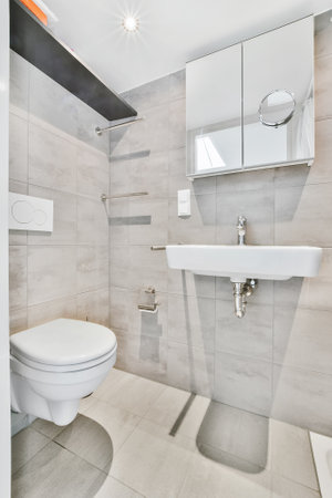 Modern small gray tiled bathroom design with shower in corner and small sink under mirror and lampの写真素材