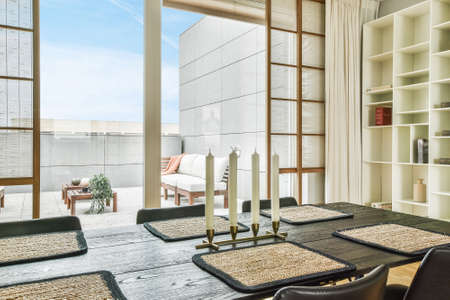Candles and placemats located against glass balcony wall in dining room of modern apartmentの写真素材