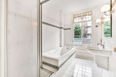 Interior design of spacious white bathroom with large bathtub and glass shower cabin and with...