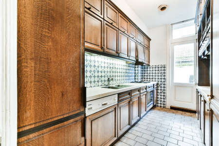 Retro style home interior design of narrow kitchen with wooden cupboards and ceramic tile walls and floorの写真素材
