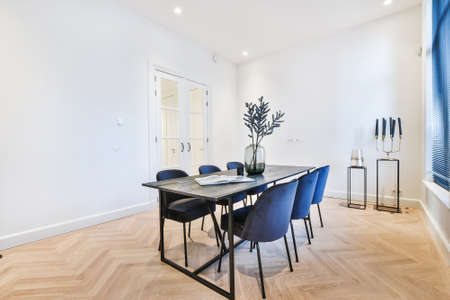 Modern dining table with set of blue velvet chairs and vase of flower on top in dining room of classic apartmentの写真素材