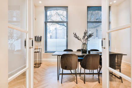 Luxury apartment dining room with parquet and black dining set against white kitchen in open plan...