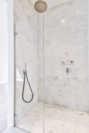 Modern spacious shower cabin with glass walls and doorway all tiled with marble tiles