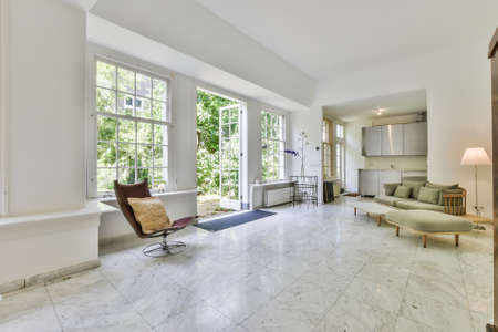 Big mansion room with tiled floor furnished with settee and armchair and small kitchen cabinets in...