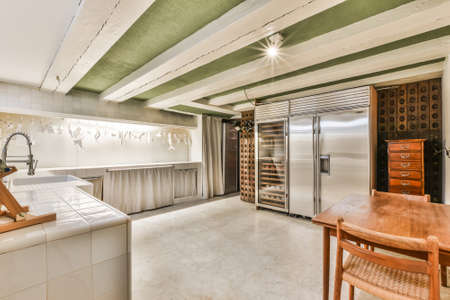 Contemporary big kitchen of mansion house with stainless fridge and wooden wine racks under white...
