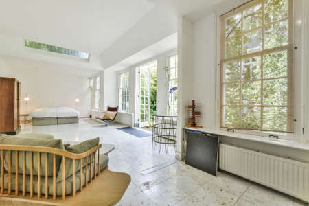 Spacious studio room with bed and wardrobe under ceiling window and opened doorway leading to green...