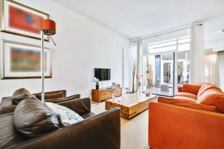 Spacious house room with sofa and armchairs against TV and design wooden table with floral vase