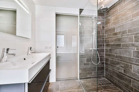 Modern design of bathroom with glass shower cabin and double basin in cabinet under mirror