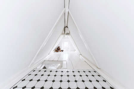 Narrow attic room with walls of conical roof decorated with tile and white paintの写真素材