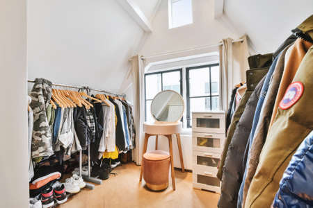 House wardrobe room with small table and pouf among racks of clothes and shoes on floorの写真素材