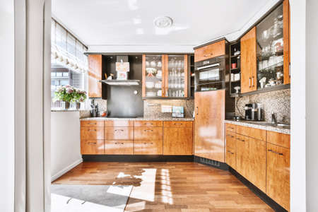 Spacious kitchen room with wooden cabinets and black elements and wooden parquet flooring in bright...