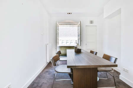 Dining table with chairs against opened window in white light room of modern house