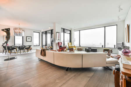 Simple interior of light living room with gray sofa and dining table against