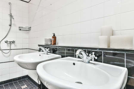 Shiny interior of bathroom tiled with black and white tiles with double sinks and open showerの写真素材