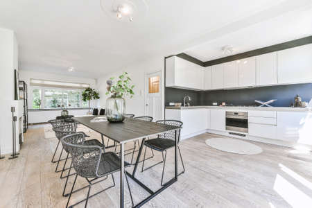Wooden table and comfortable chairs placed near kitchen furniture in modern light flat