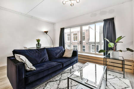Comfortable sofa with soft cushions located under stylish chandelier in spacious light living room