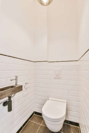 Wall hung toilet and small sink in corner in lavatory room with light tileの写真素材