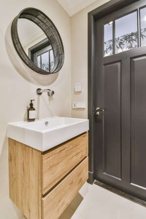 Bathroom corner with stylish sink and round mirror in black frame next to the door