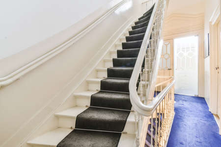 White hallway with wooden stairway leading to second floor of modern luxury apartment with minimalist interior designの写真素材