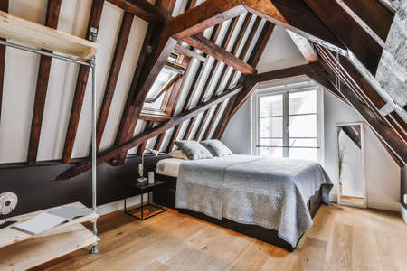 Stylish attic bedroom with wooden beams and a soft bedの写真素材
