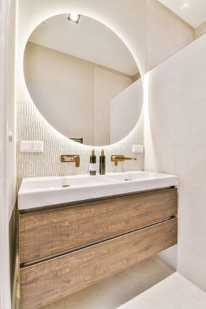 Stylish bathroom with large round illuminated mirror and two sinksの写真素材