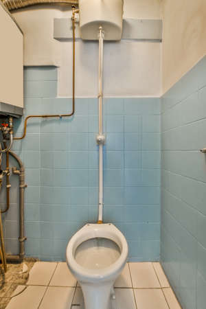 A small, old-fashioned toilet with a blue tile and lots of pipes