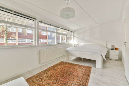 A small bedroom with a double bed in a white design and a carpet on the floor in a modern house