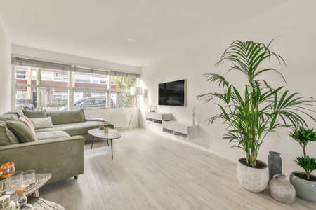 The interior of a modern spacious living room with a corner green sofa on a parquet floor