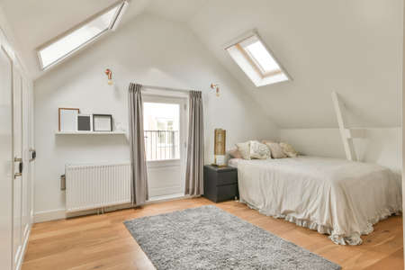 The interior of a cozy bedroom with slanted windows on the ceiling and a carpet on the floorの写真素材