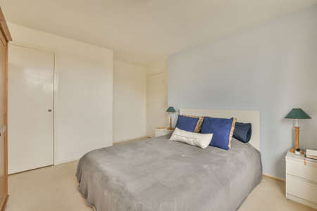 A bedroom with a bed with a grey bedspread, carpet on the flooor in a modern house