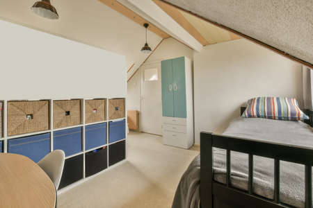 A bedroom with a bed with a grey bedspread, carpet on the flooor and colorful lockers in a modern...