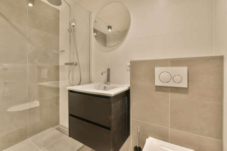 The interior of the bathroom with a shower stall and a ceramic sink under a round mirror