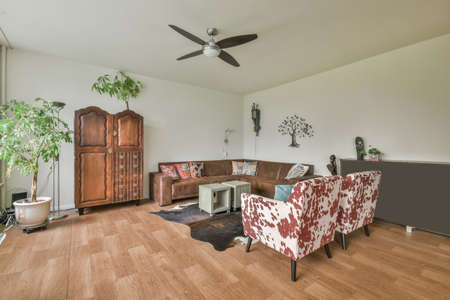 Cozy living room with sofa, armchairs, carpet and wardrobe in brown tones in a modern house
