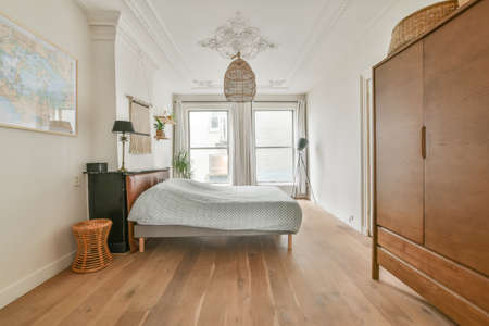 The interior of a spacious bedroom with a large bed and a wooden wardrobe next to itの写真素材