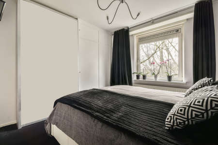 The interior of a bedroom with a black and gray design and a large window in a cozy apartmentの写真素材