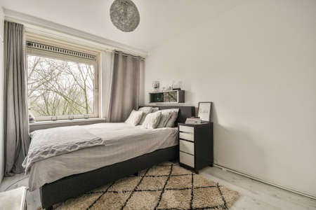 The interior of a bedroom with a gray and white design and a large window in a cozy apartment