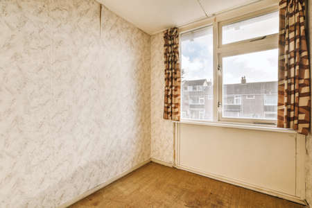 The interior of a spacious empty room with a bright window and wallpaper on the walls in a cozy...