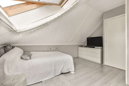 The interior of a modern bedroom with a large bed and a TV next to the wondowの写真素材