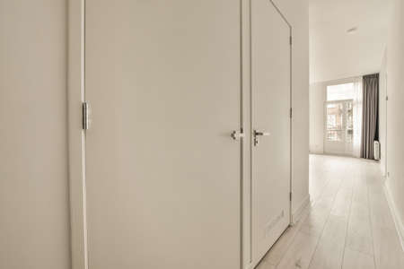 Design of a white narrow corridor leading to an apartment with laminate flooring