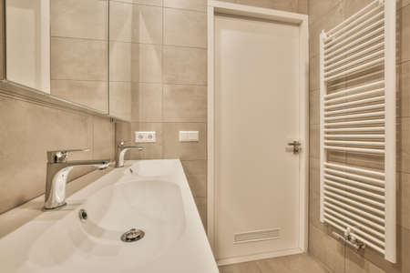 The interior of a modern bathroom made of beige tiles with a double ceramic under the mirror