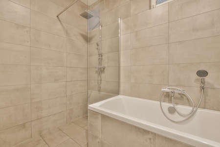 The interior of a modern bathroom made of beige tiles with a bathtub and a shower cabin