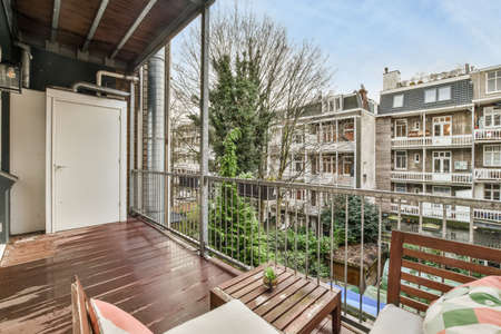 A spacious balcony with wooden floors and furniture with a seating area and a view of the courtyard...