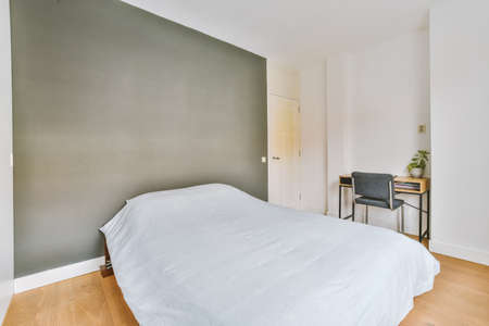 The interior of a bedroom with a bed, a workplace and a small laptop in a modern apartment