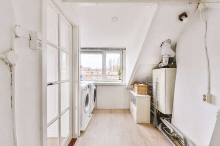 Interior of bright mansard laundry room with white walls and wooden parquet with window and doorの写真素材