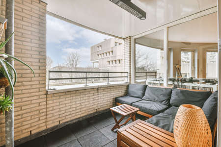 A spacious balcony in a residential building with tiled floors and a cozy dark-colored sofa