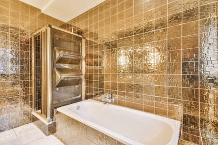 Shower faucets attached to tiled wall near bathub and glass partition and ornamental curtail in...