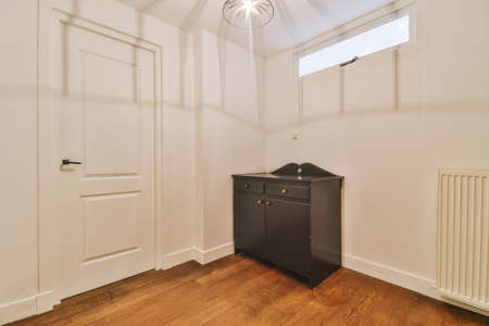 A small empty room in a modern house with a wooden brown cabinet on a parquet floor