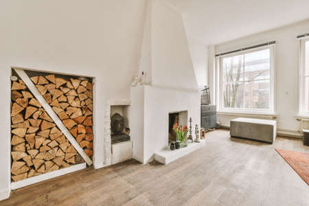 A spacious bright living room with a fireplace and a supply of firewood next to several panoramic...