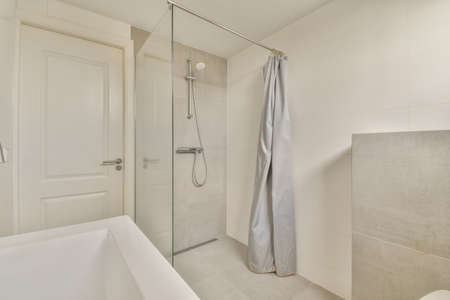 Shower faucets attached to tiled wall near glass partition and ornamental curtail in washroom at...